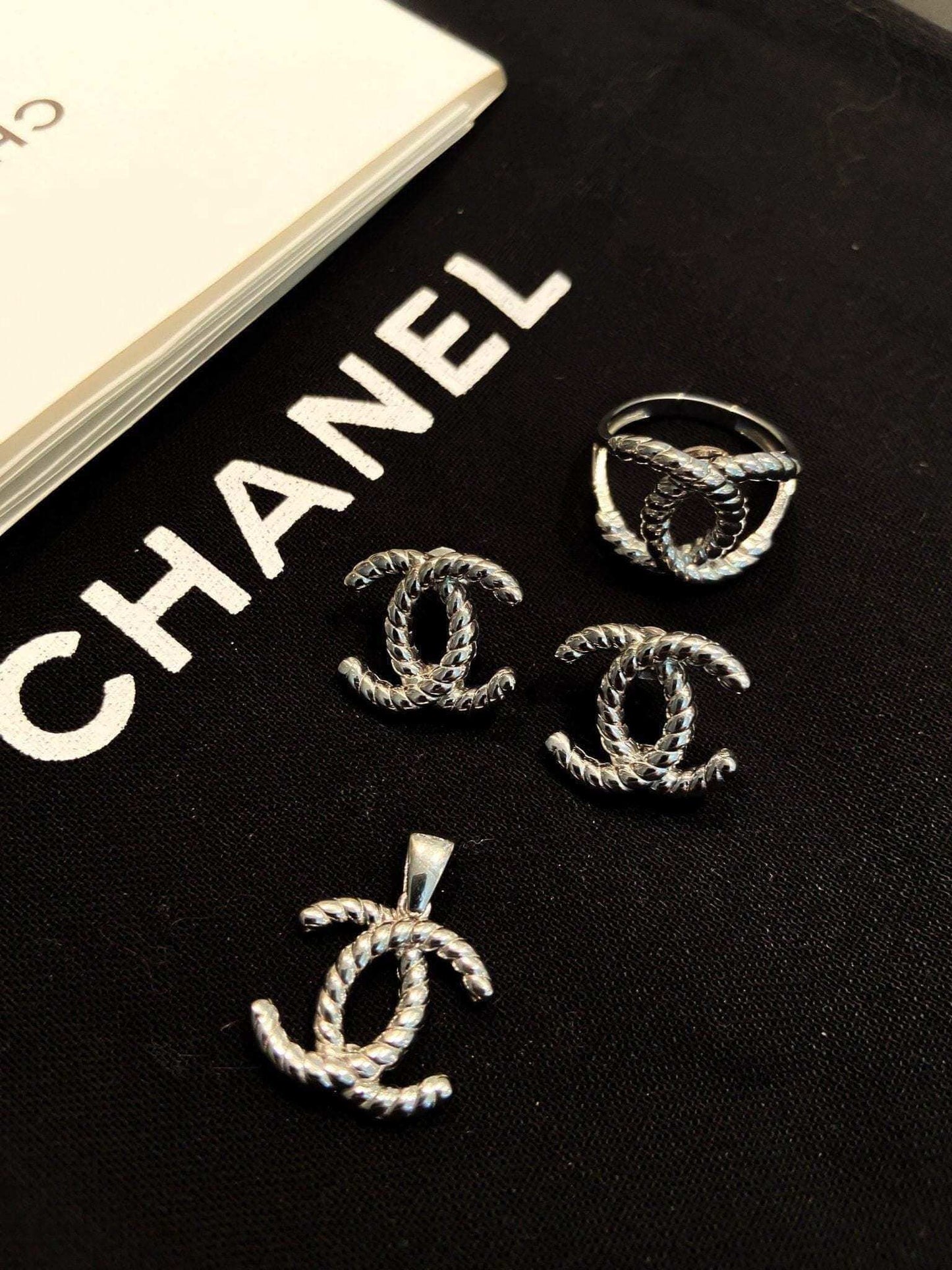 Vintage Chanel Set 925 sterling silver earrings ring and pendant on black background with Chanel logo text