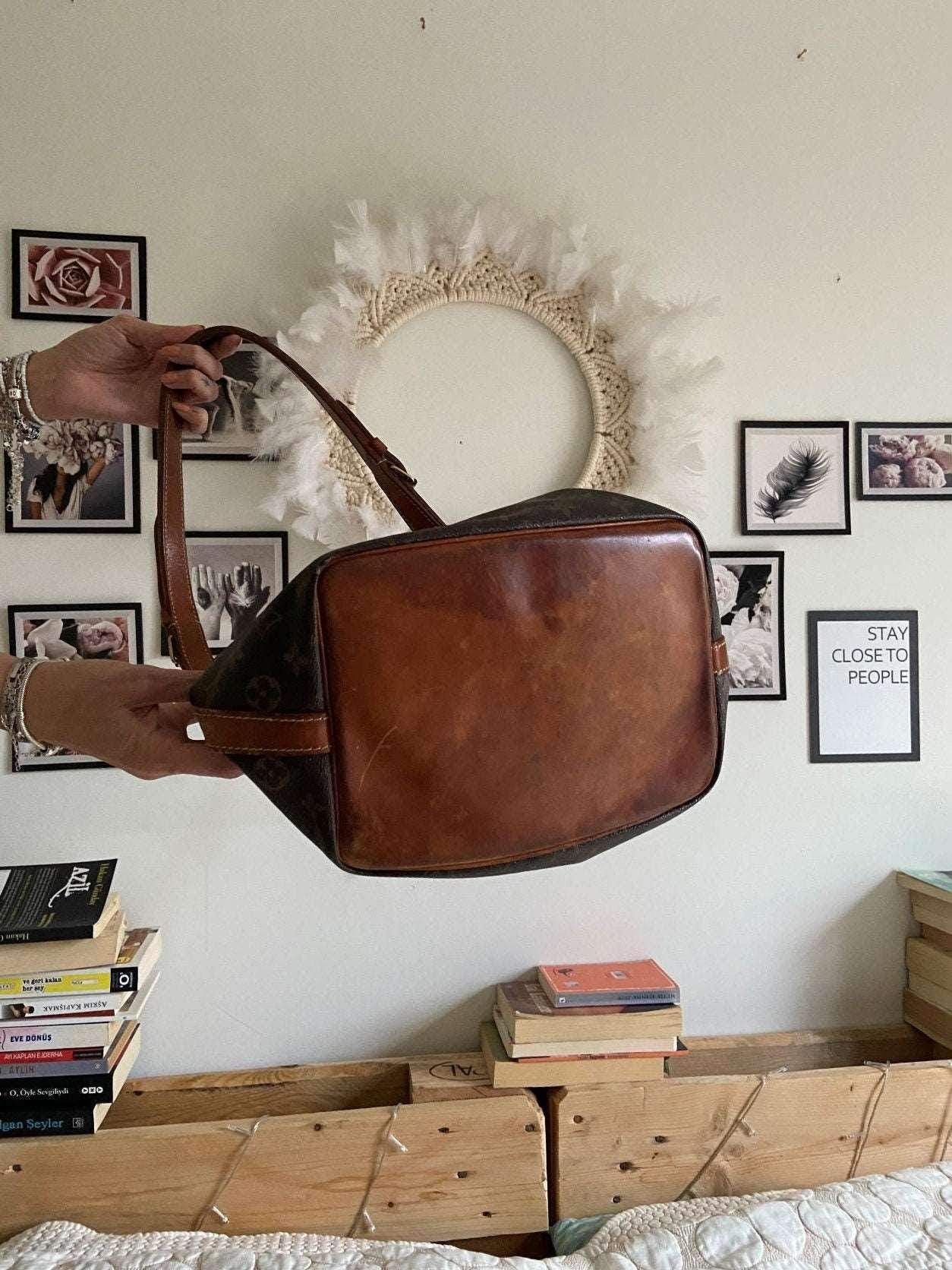 Authentic vintage Louis Vuitton Noe bag with monogram and worn leather base held by hands indoors