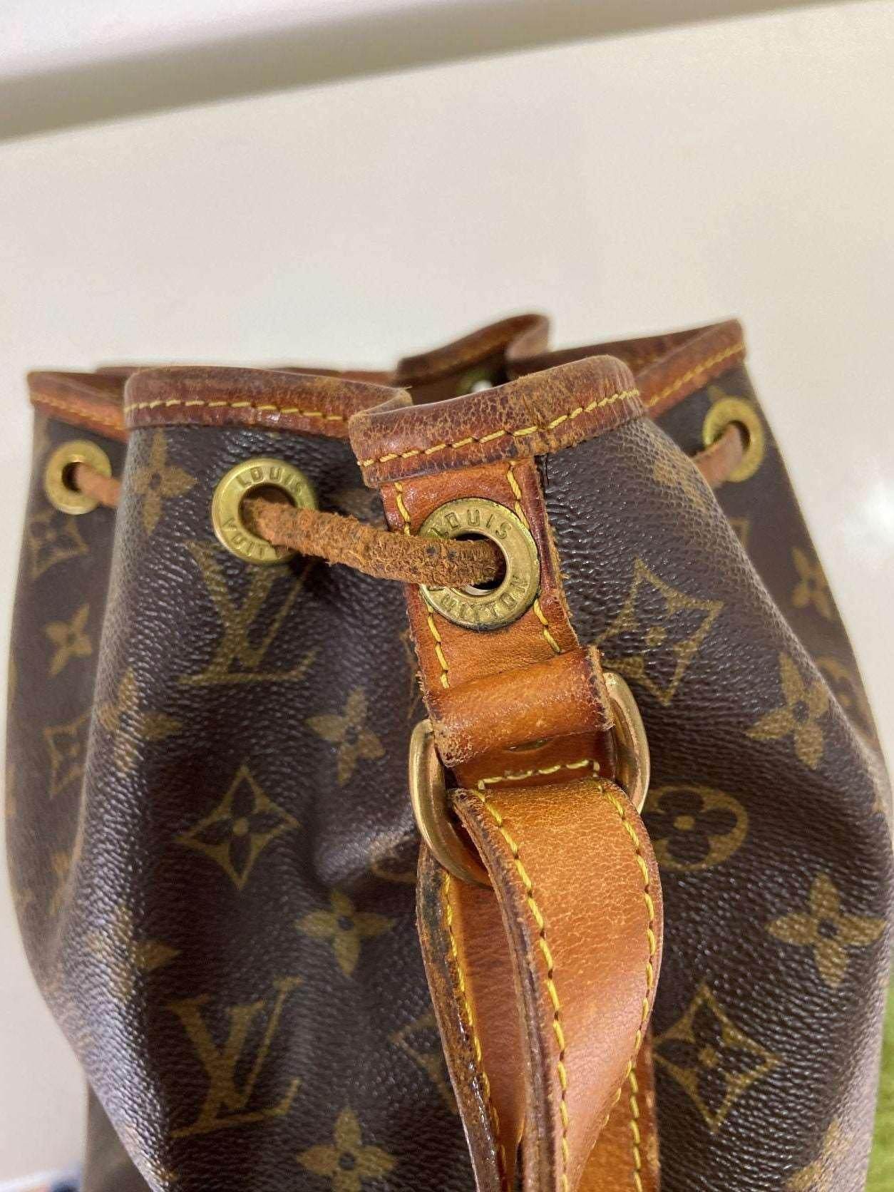 Close-up of authentic Louis Vuitton Noe bag monogram with leather strap and brass eyelets showing wear and vintage condition