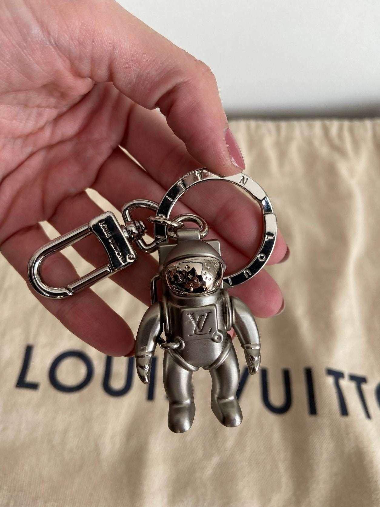 Louis Vuitton Astronaut Keychain MP2213 Silver metal charm with bag ring and clip in hand over Louis Vuitton dust bag